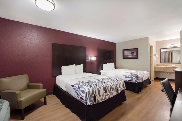 A hotel room with two beds, a desk, a chair, a mirror, and a picture on the wall.
