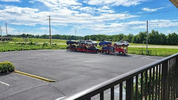 Um estacionamento com uma caminhonete vermelha transportando carros em um reboque, cercado por vegetação e um céu claro.
