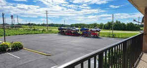 A parking lot with a red truck transporting cars on a trailer, surrounded by greenery and a clear sky. - Red Roof Inn Bishopville (Bishopville)