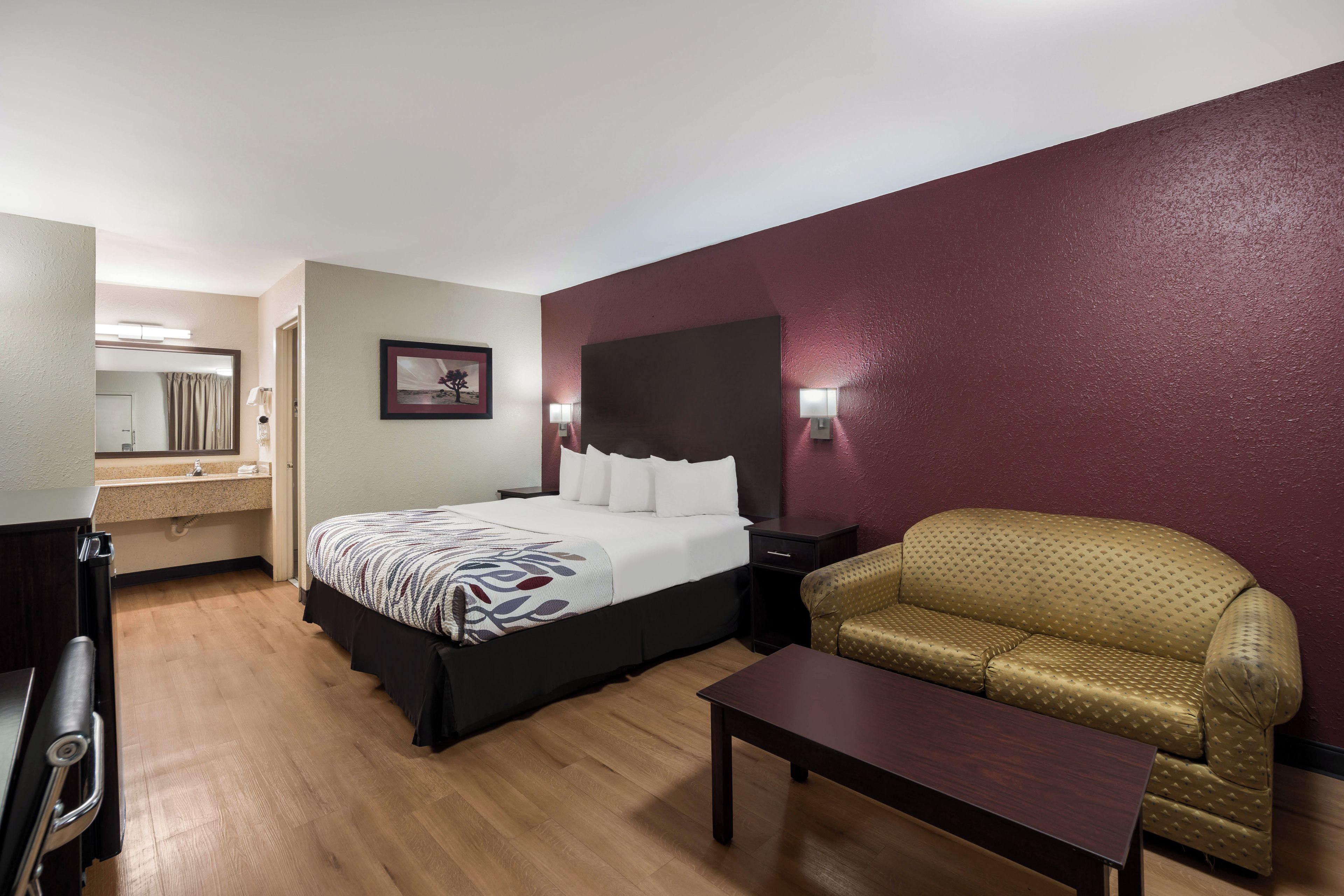 Habitación de hotel con cama, sofá, mesa, espejo y un cuadro en la pared.