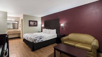 Quarto de hotel com cama, sofá, mesa, espelho e um quadro na parede.