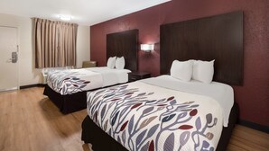 A hotel room with two beds, dark wooden headboards, a large mirror, and a beige curtain.