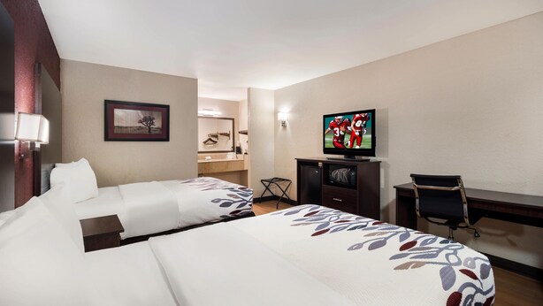 A hotel room with two beds, a television, a desk, and a chair.