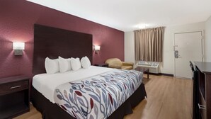A hotel room with a large bed, a bedside table, a chair, a desk, and a wardrobe.