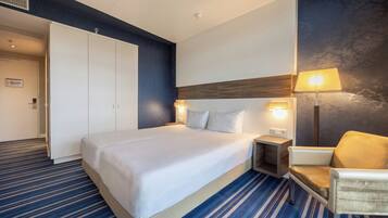 Habitación de hotel con una cama grande, lámparas de noche, una silla y un armario.