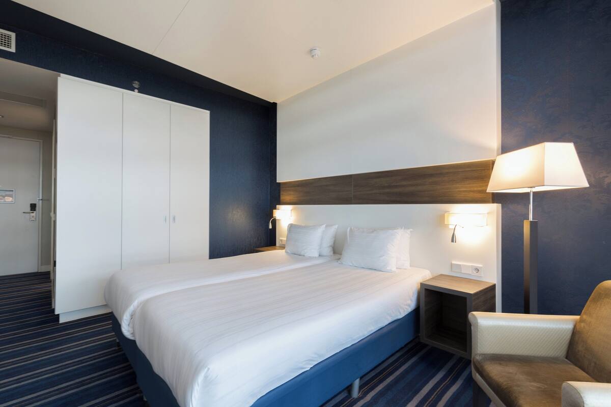 Une chambre d’hôtel avec un grand lit, une chaise, une table de chevet et une lampe.