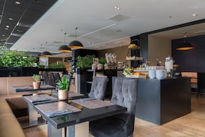 A modern restaurant with a central bar area, seating arrangements, and various plants. - Leonardo Royal Hotel Den Haag Promenade (The Hague)