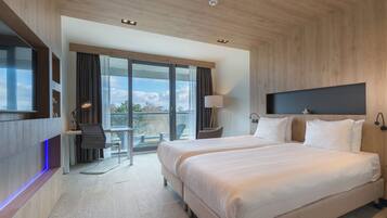 A modern hotel room with two beds, a desk, and a large window offering a view of the outdoors.