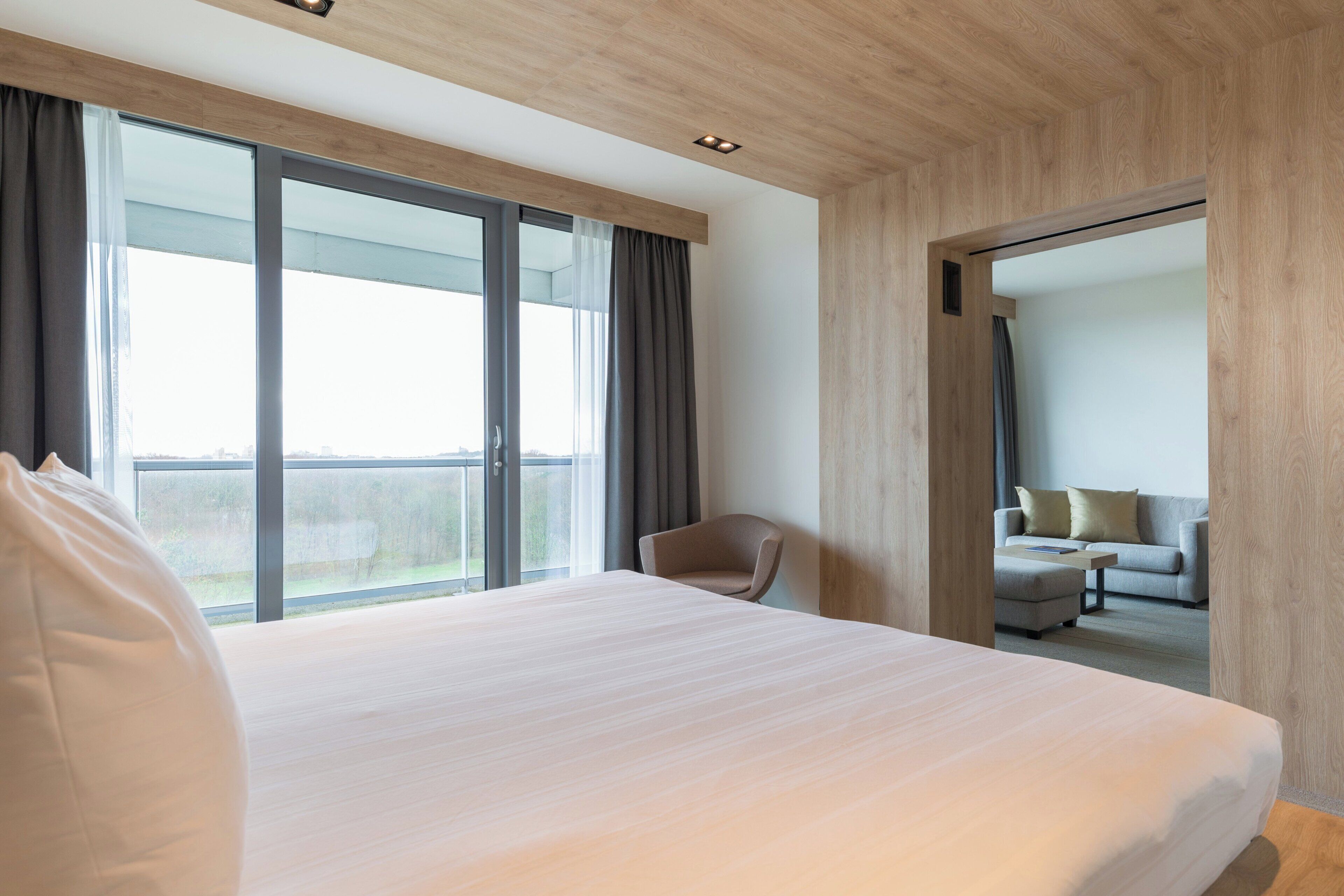 Una habitación de hotel moderna con una cama grande, una silla, un sofá y un balcón con cortinas.