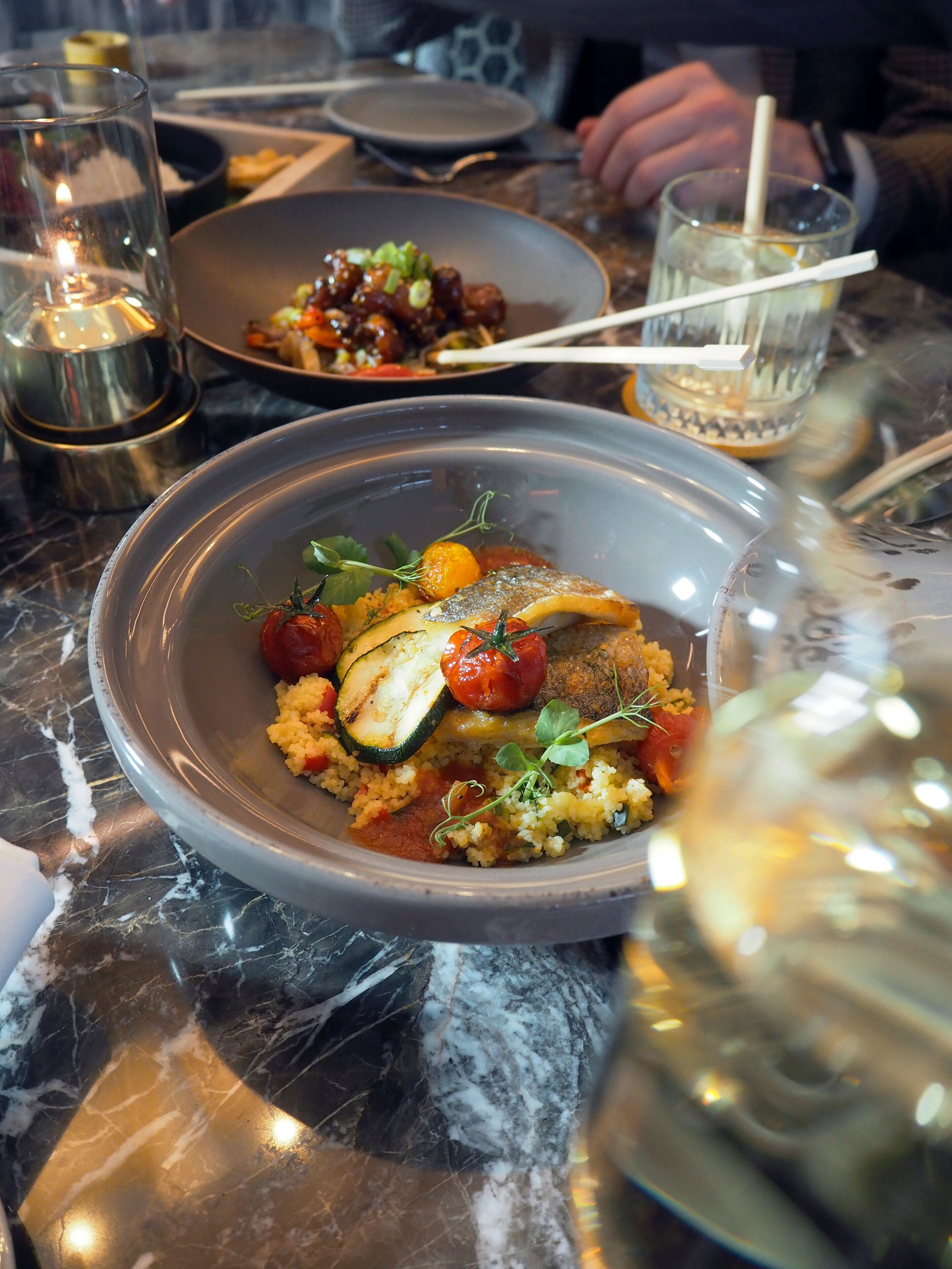 A dining table with a bowl of food, a glass of water, and a candle.