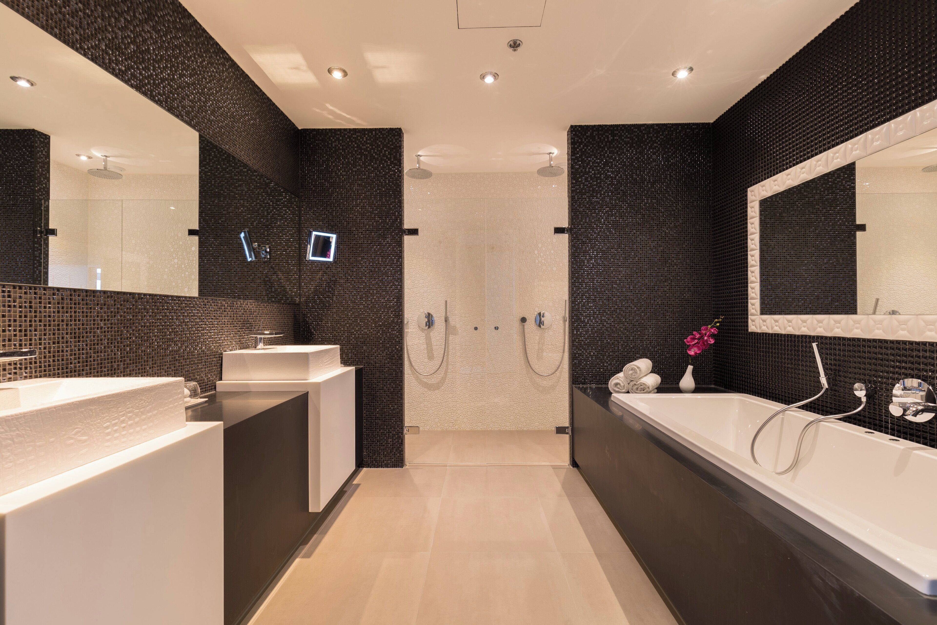 Une salle de bain moderne dotée d’un grand miroir, de deux lavabos, d’une baignoire et d’un espace douche.