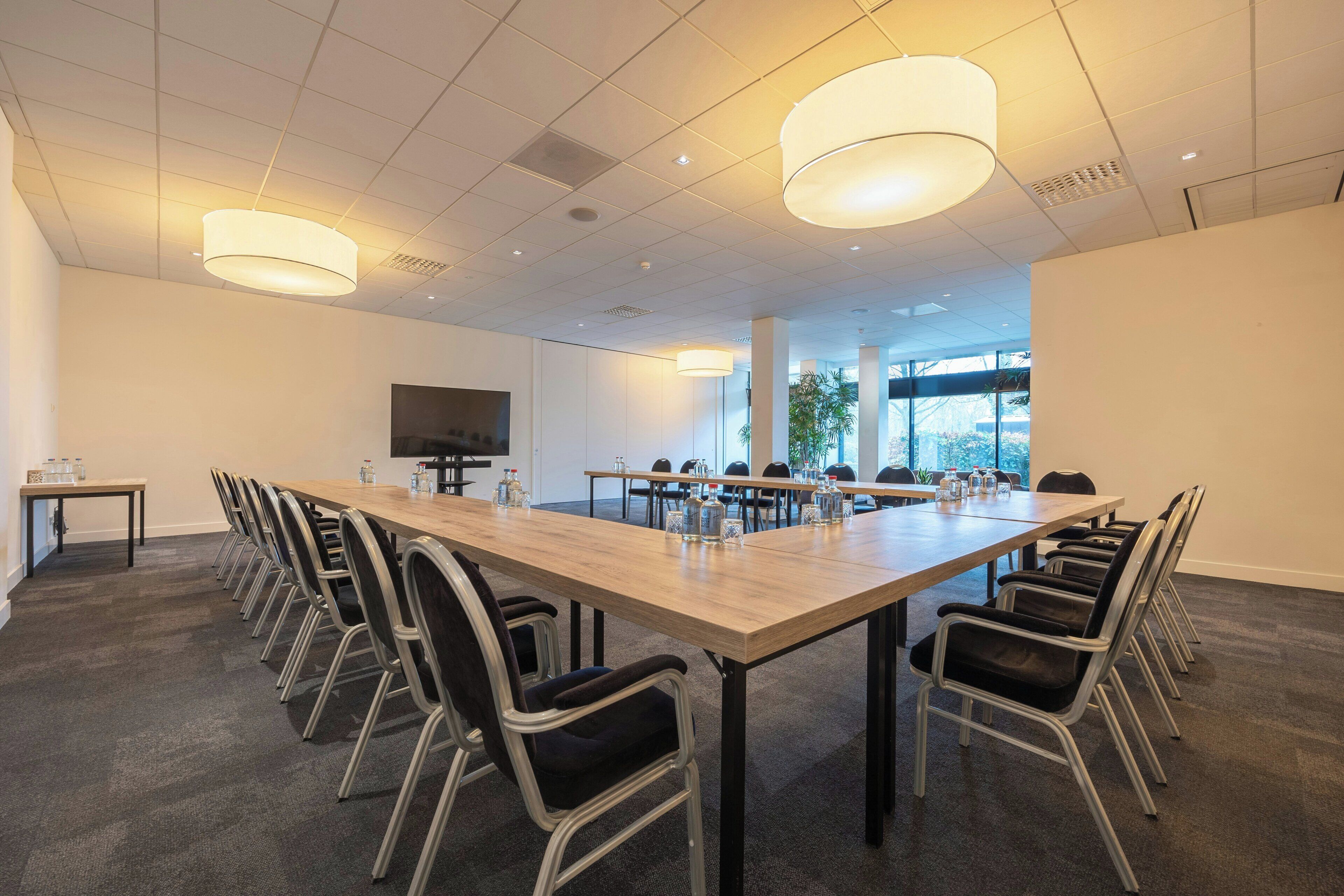 Une salle de conférence avec une longue table, des chaises et un téléviseur.