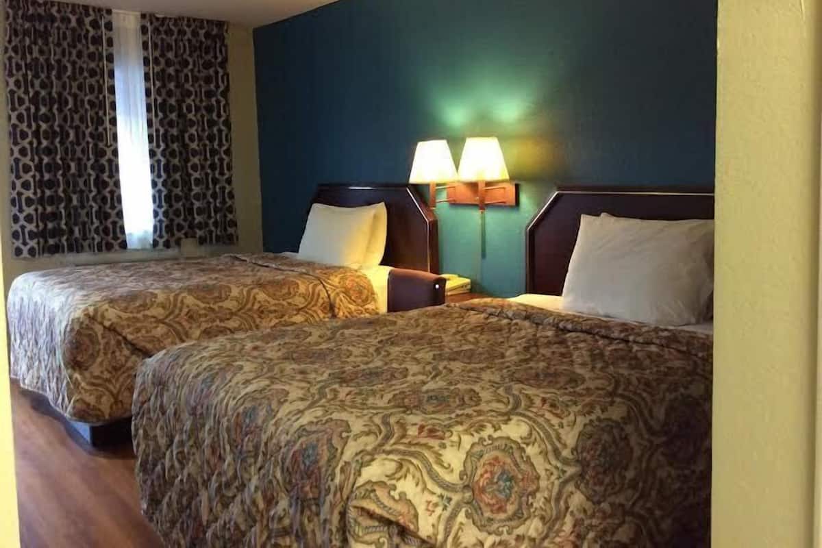 A hotel room with two beds, patterned bedspreads, a nightstand with a lamp, and a window with patterned curtains.