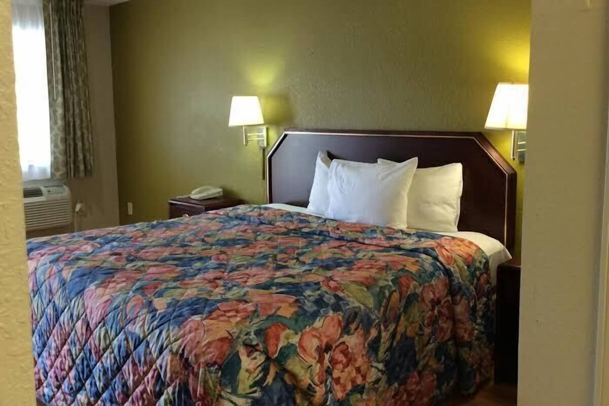 A hotel room with a bed, two bedside lamps, a nightstand, and a window with curtains.