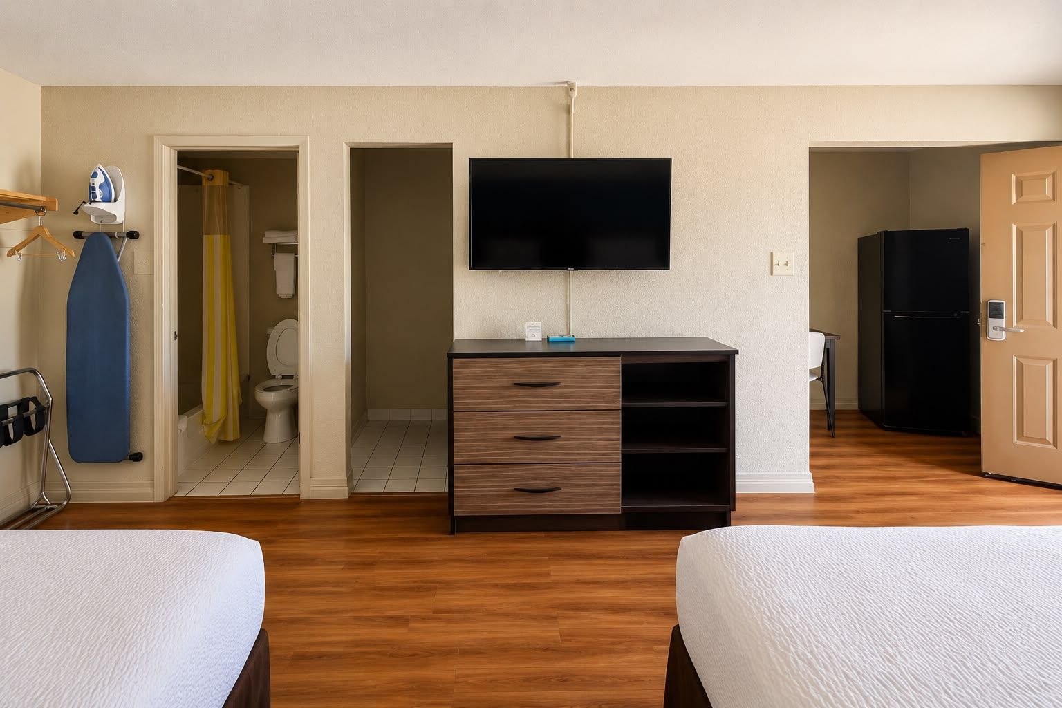 A hotel room with two beds, a TV, a wardrobe, and a bathroom visible through an open door.