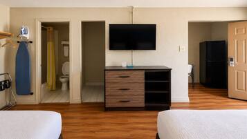 A hotel room with two beds, a TV, a wardrobe, and a bathroom visible through an open door.