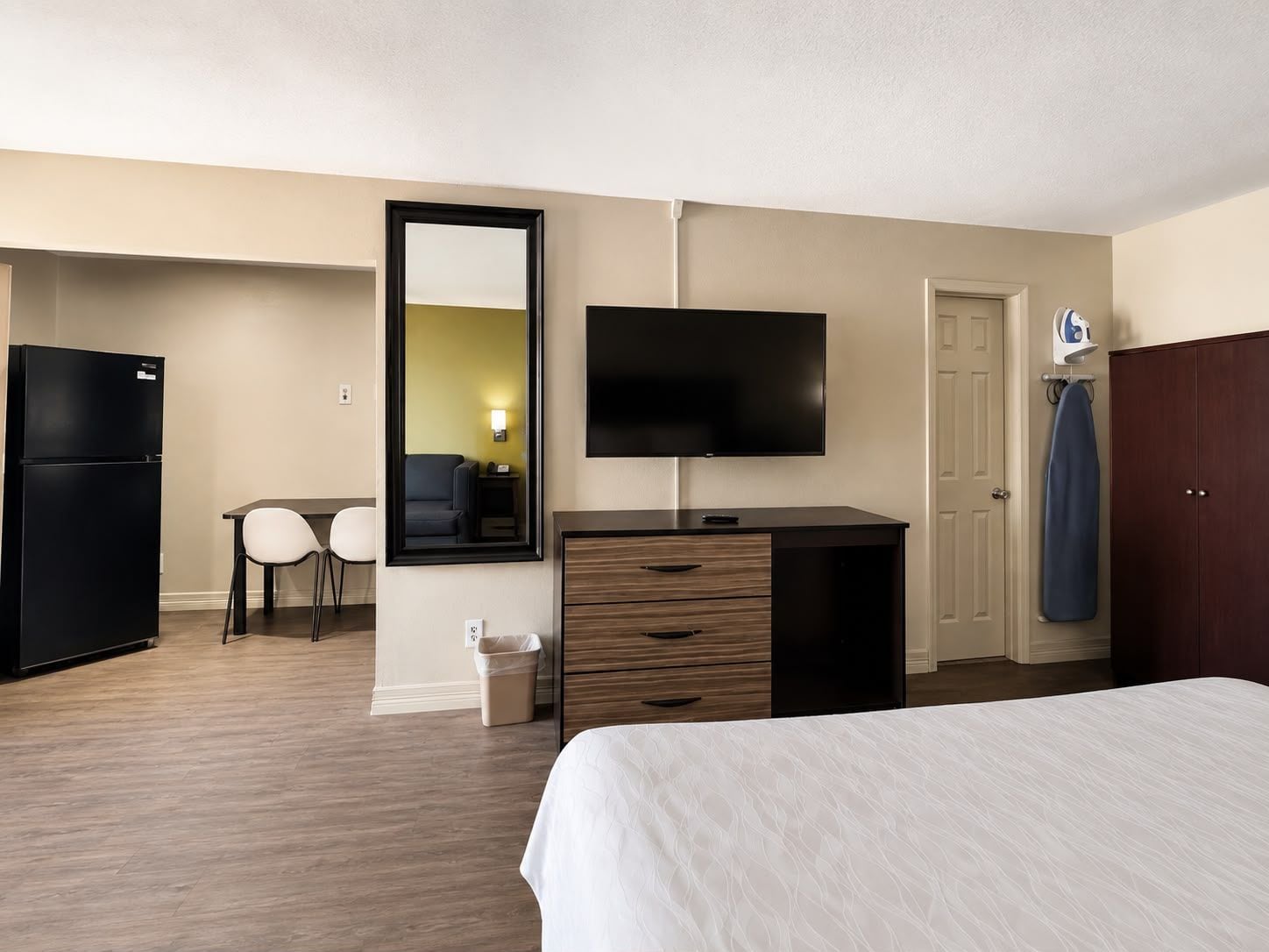 A hotel room with a bed, a desk with a chair, a television, a wardrobe, and a refrigerator.
