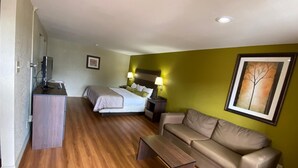 A hotel room with a bed, a sofa, a desk with a computer, and a painting on the wall. - Stratford House Inn and Suites (Temple)