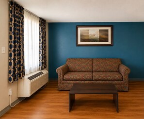 A living room with a patterned sofa, a coffee table, and a framed picture on the wall. - Stratford House Inn and Suites (Temple)