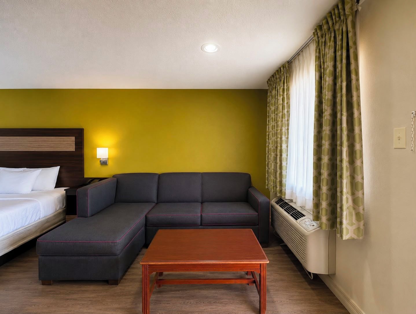 A hotel room with a bed, a sofa, a small table, and a heater.