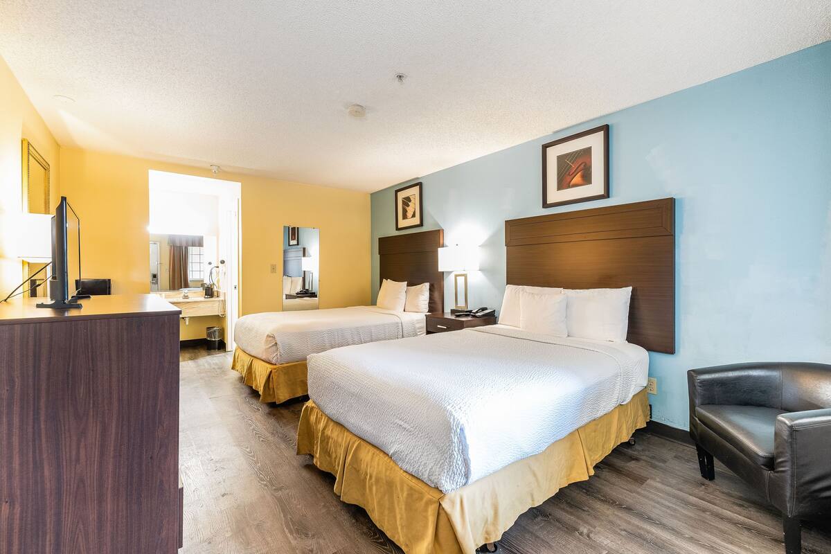 A hotel room with two beds, a desk, a chair, and a TV.