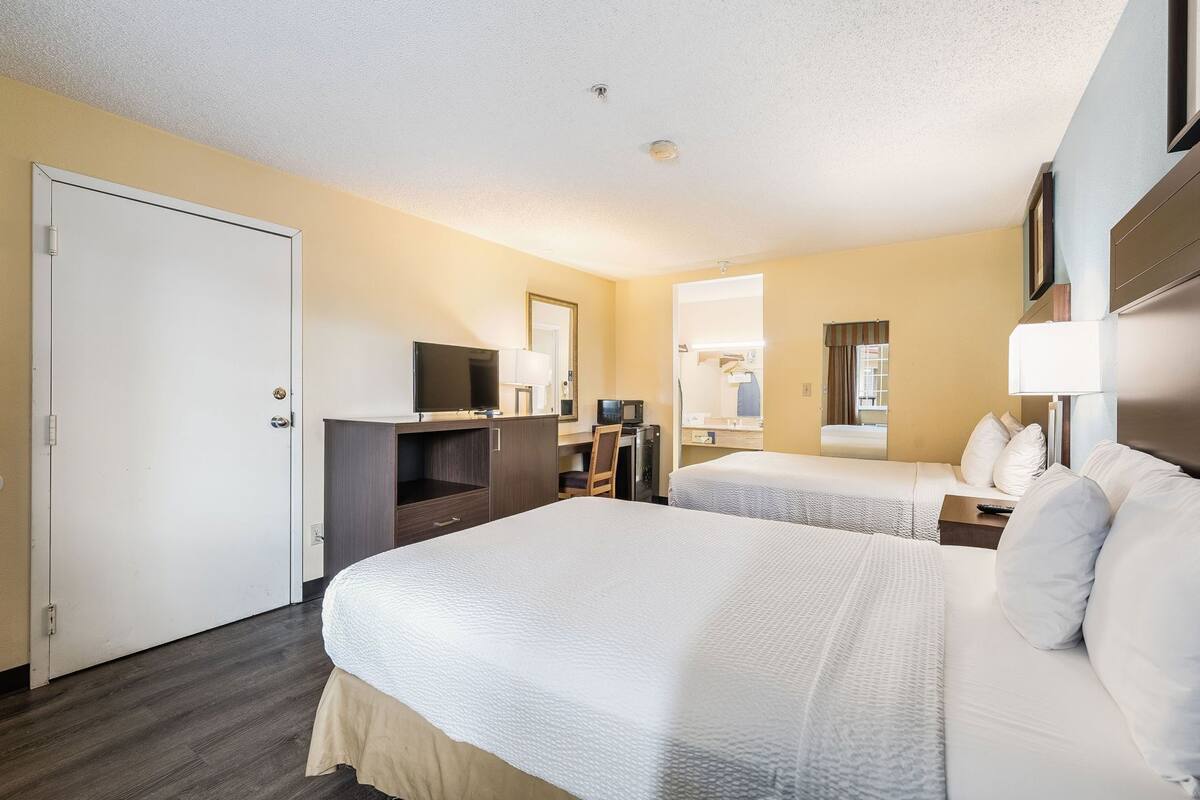 A hotel room with two beds, a desk with a computer, a TV, and a mirror.