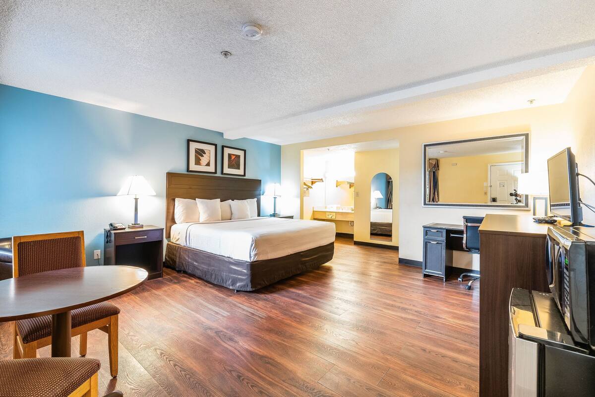 A hotel room with a bed, a desk, a chair, a dining table, and a kitchenette.