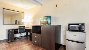 Une chambre d’hôtel équipée d’un bureau en bois, d’une chaise, d’un grand miroir, d’un téléviseur à écran plat et d’un four à micro-ondes intégré.