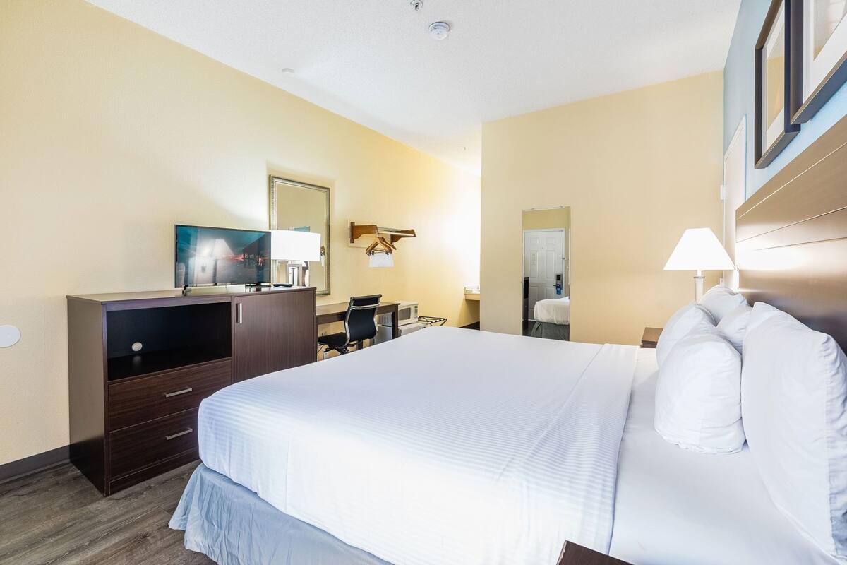 A hotel room with a large bed, a desk with a chair, a television, a mirror, and a bedside lamp.