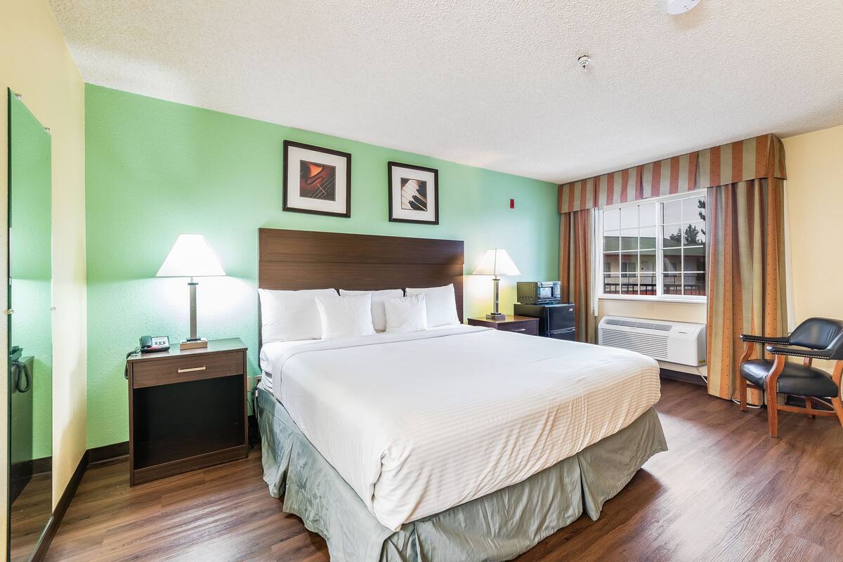A hotel room with a large bed, two bedside tables with lamps, a wooden headboard, and a window with curtains.
