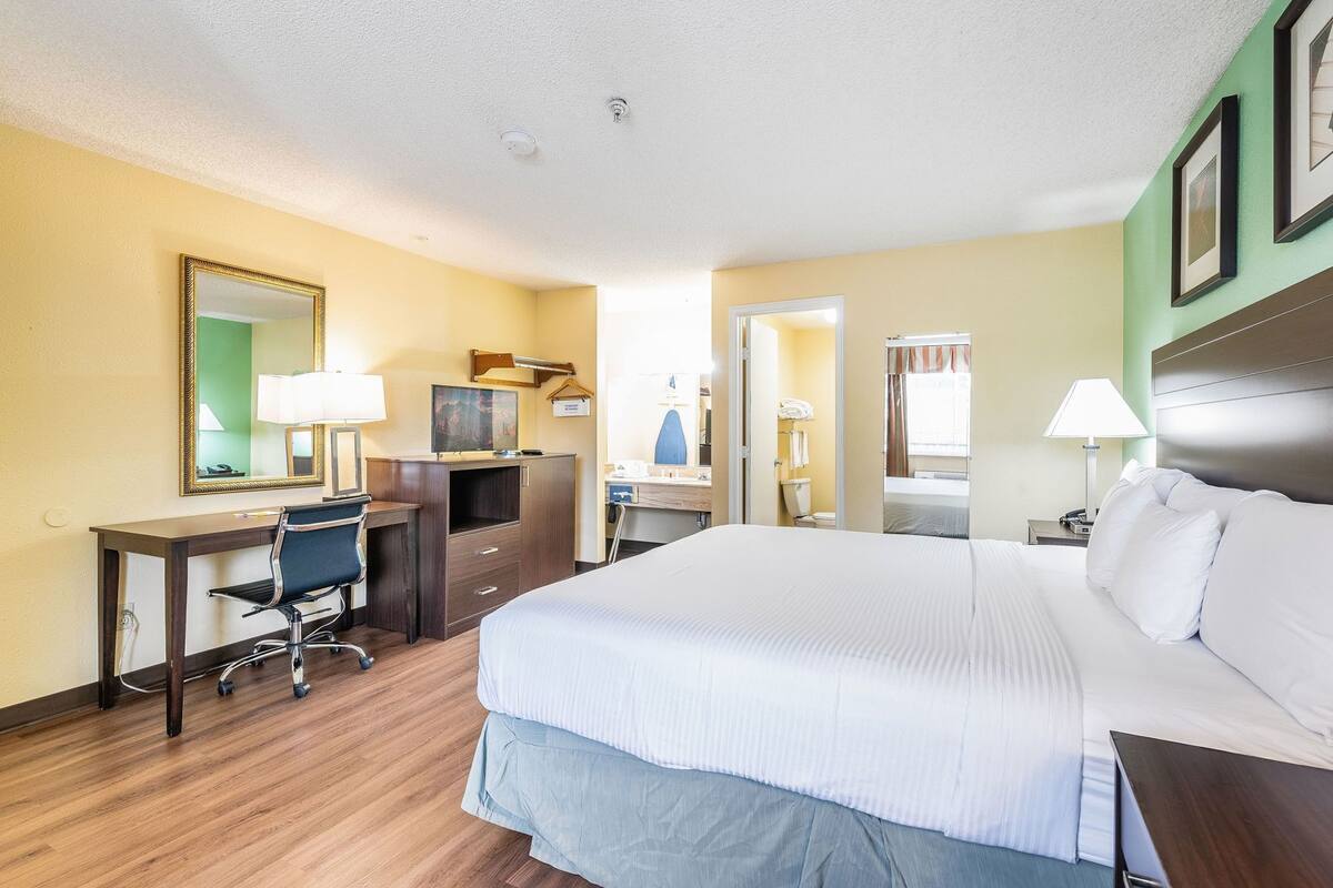 A hotel room with a bed, desk, chair, and a mirror.