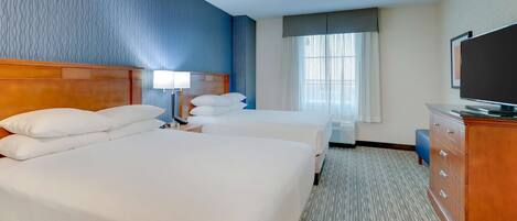 A hotel room with two beds, a television, a desk with a lamp, and a window with curtains.