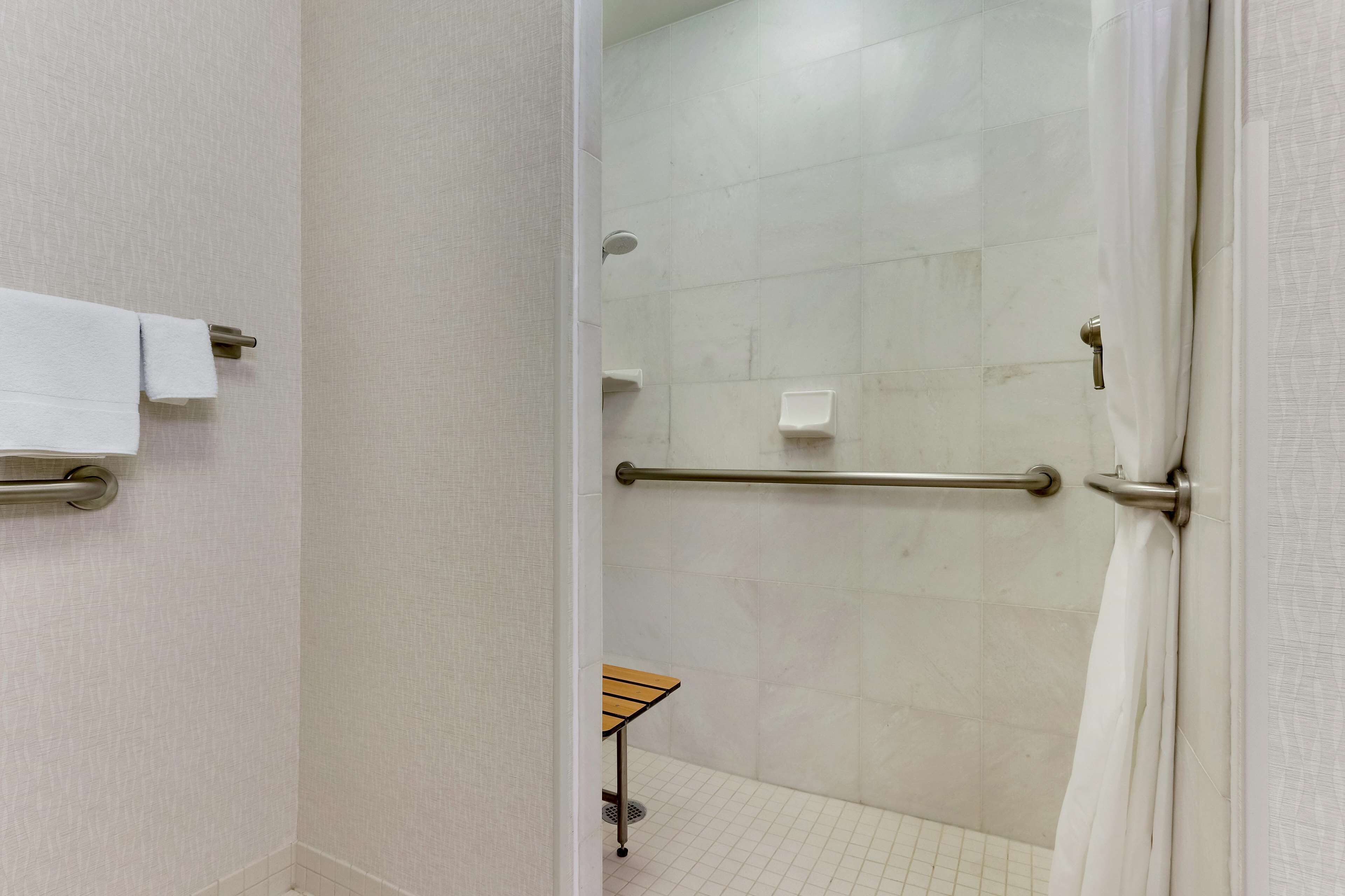 Un baño con ducha, barras de apoyo, un perchero y una mesita.