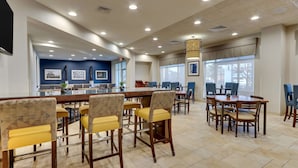 A spacious dining area with high tables and chairs, a bar counter, and large windows providing natural light. - Drury Inn & Suites Sikeston, MO (Sikeston)