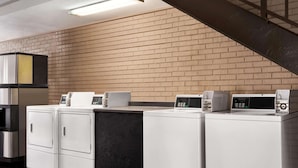 A laundry area with stacked washers and dryers, a brick wall, and a staircase. - Super 8 by Wyndham Gulfport Airport NW/Near Biloxi (Gulfport)