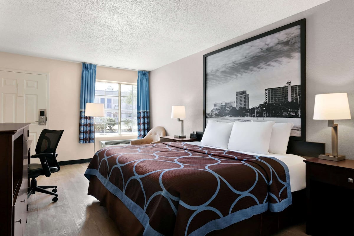 Habitación de hotel con una cama grande, dos lámparas de noche, un escritorio con silla y un cuadro de un paisaje urbano en la pared.