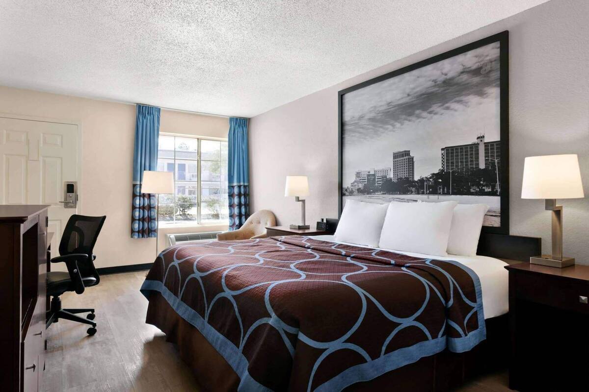 Una habitación de hotel con una cama grande, dos lámparas de noche, una silla, un escritorio y una ventana con cortinas.