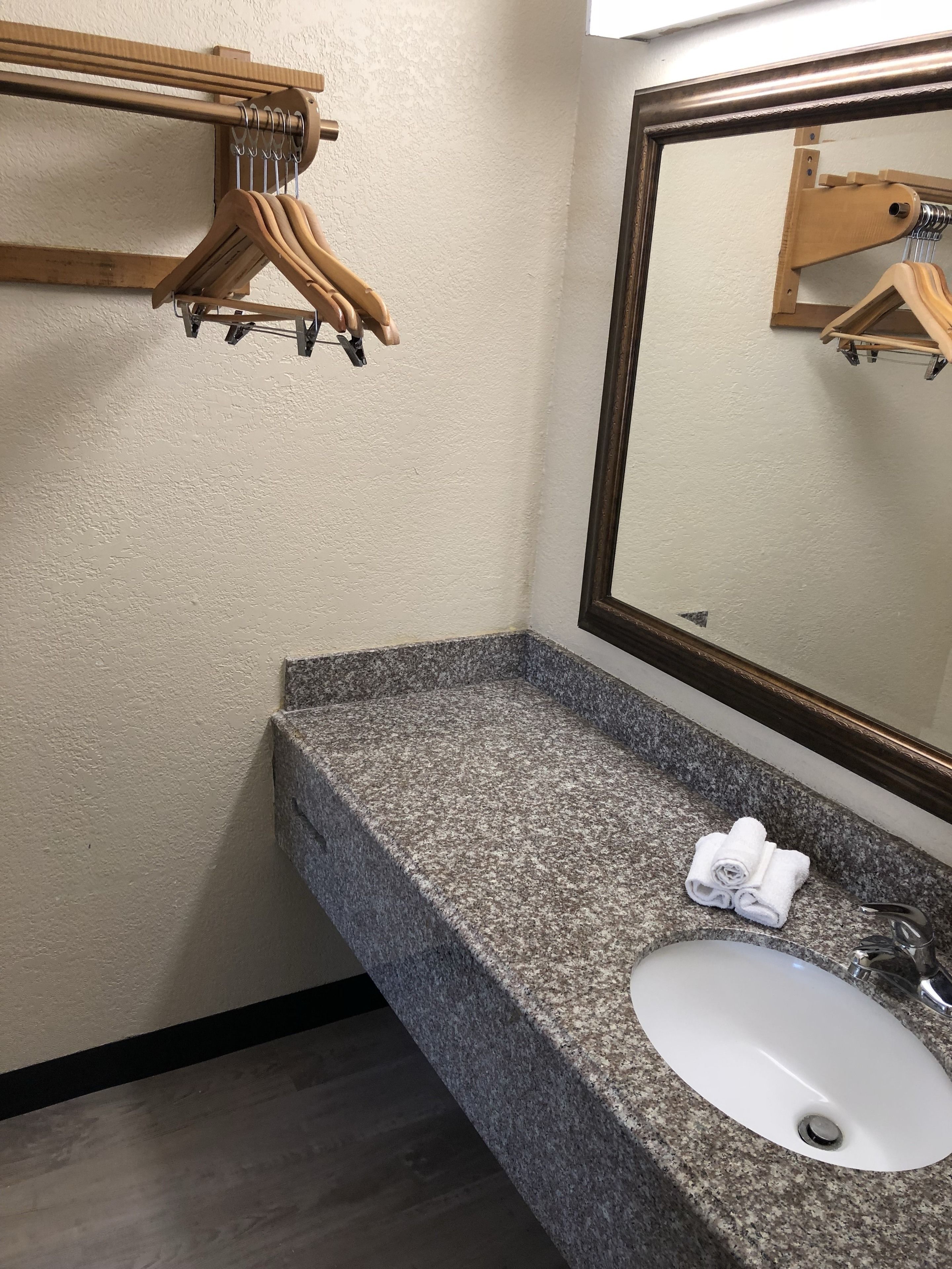 A bathroom with a granite countertop, a white sink, and a wooden towel rack.