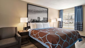 A hotel room with a large bed, two bedside lamps, a chair, a framed cityscape picture, and a window with curtains. - Super 8 by Wyndham Gulfport Airport NW/Near Biloxi (Gulfport)