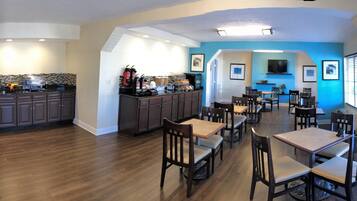 A spacious kitchen with dark wooden cabinets and a black countertop, a dining area with wooden tables and chairs, and a blue accent wall.