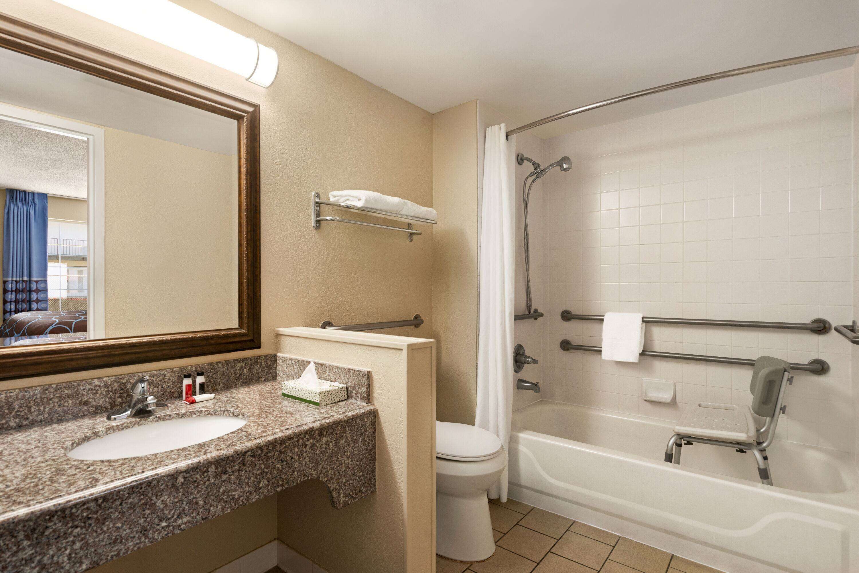 A bathroom with a granite countertop sink, a mirror, a toilet, and a walk-in shower with grab bars.