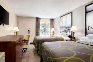 A hotel room with two beds, a desk, a chair, a TV, and a window with curtains.