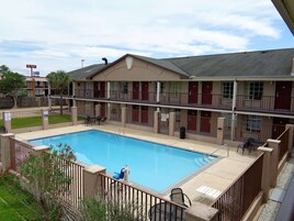 A two-story motel with a swimming pool, outdoor seating, and a fenced patio area.