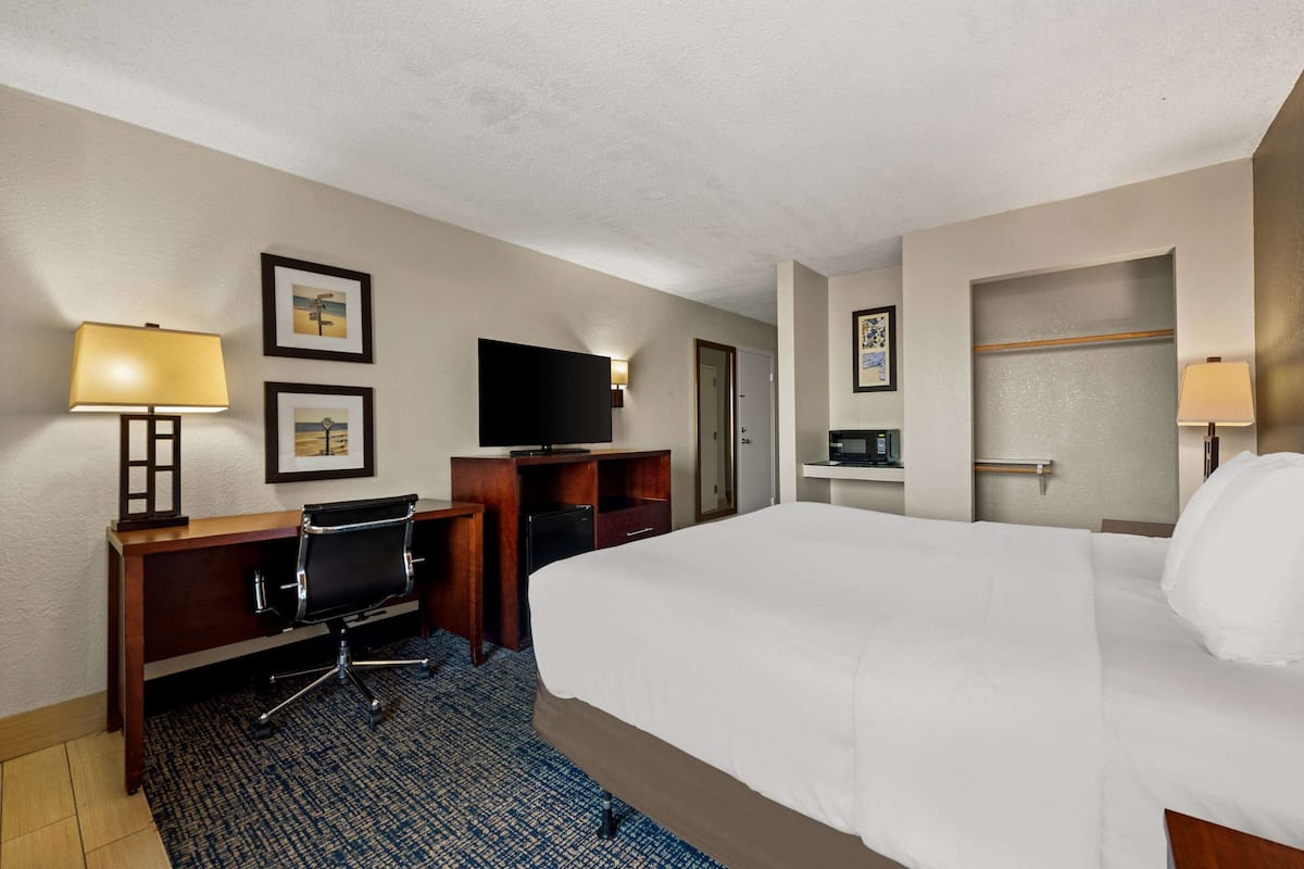 A hotel room with a large bed, a desk with a chair, a television, and a small refrigerator.