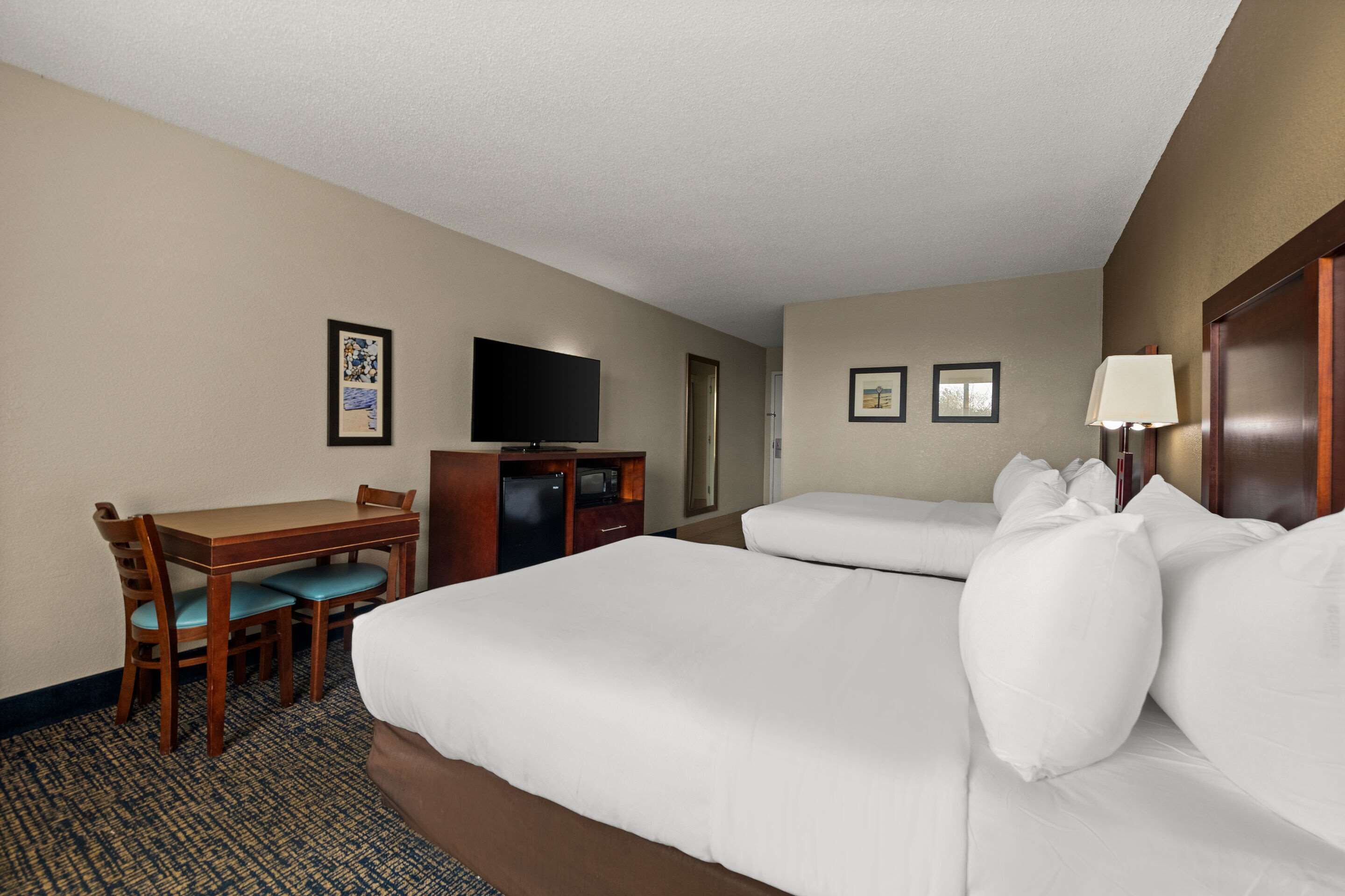 A hotel room with a bed, a desk with a chair, a television, and a lamp.