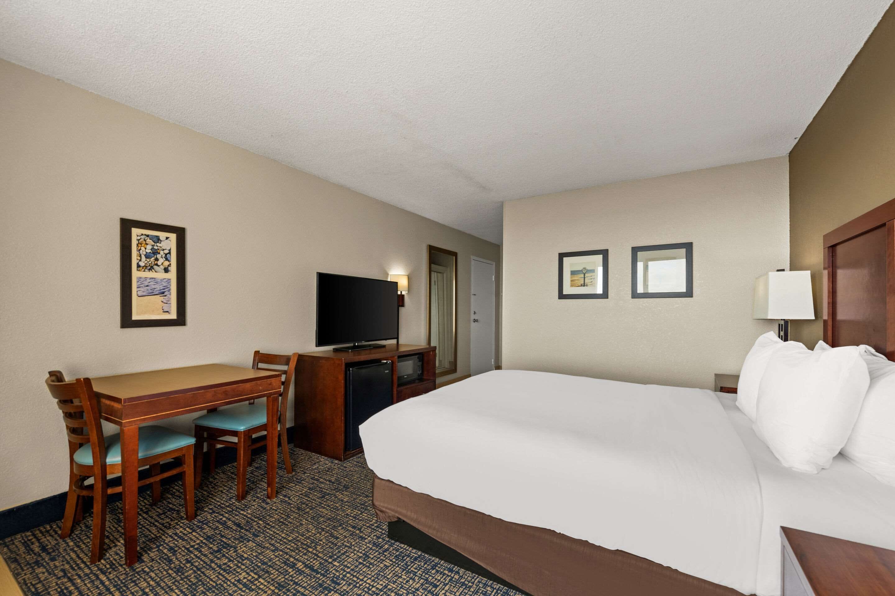 A hotel room with a bed, a desk with a television, and two framed pictures on the wall.