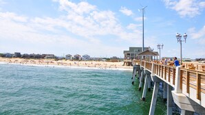 A pier extending into a beach with people walking and sitting.