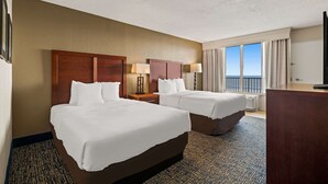 A hotel room with two beds, a desk, a chair, a TV, and a window with a view.