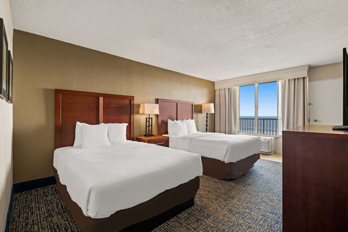 A hotel room with two beds, a desk, a chair, a TV, and a window with a view.