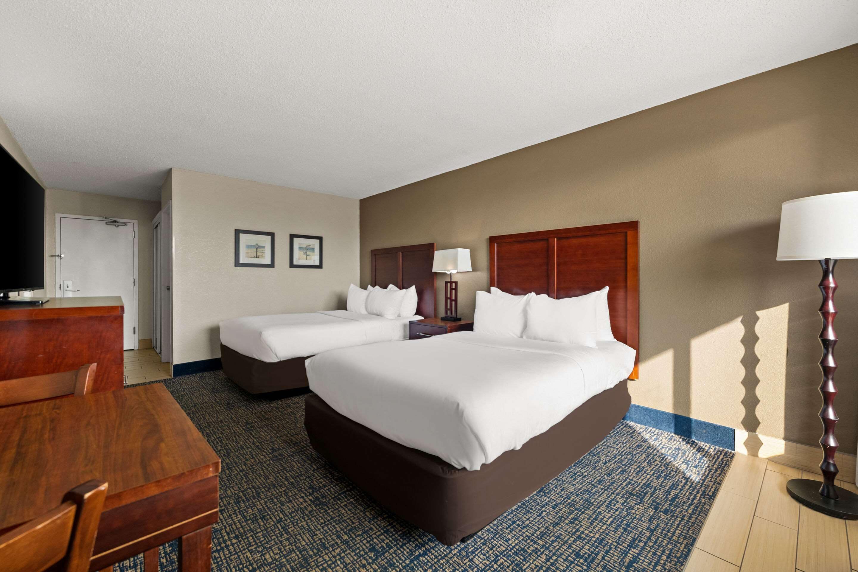 A hotel room with two beds, a desk, and a television.